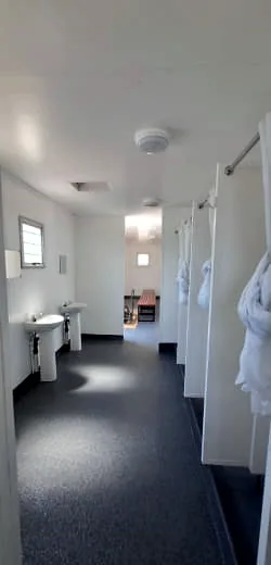 Ablution room with two pedestal basins on one side and curtained shower stalls on the other, leading to a doorway.