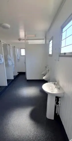 Ablution room with a pedestal basin, wall urinals, shower stalls and windows along one wall.