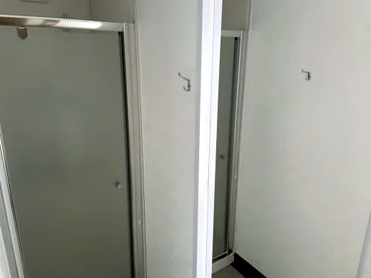 Shower cubicles with frosted glass doors in aluminium frames and a towel hook on the white wall.