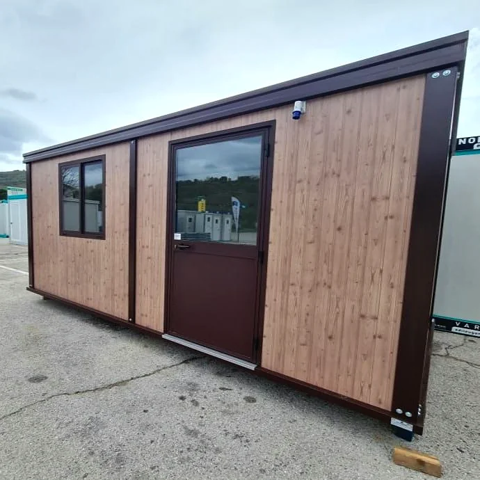 Angled view of a portable cabin with timber-look cladding, brown trim, a half-glazed door and a side window.