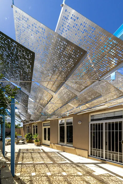 Perforated metal shade canopy over a building walkway.