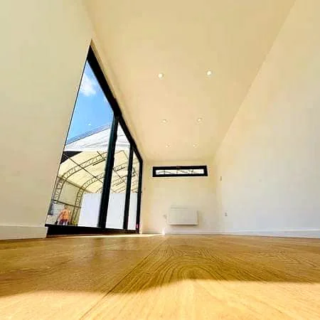 Finished interior with smooth white walls, timber-look flooring, downlights, a wall heater panel and a full-height glass wall.