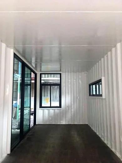 Interior of a shipping container with white-painted corrugated walls, glass sliding doors on one side, an end window and a small side window.