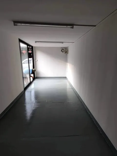 Narrow container interior with white walls, glossy grey floor and a glass door.