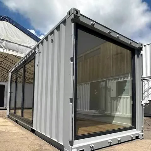 Grey shipping container office with a full-height glazed end and glass panels along the side.