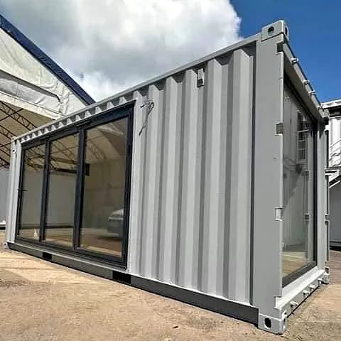 Grey shipping container office with a row of black-framed glass panels along the side and a glazed end.