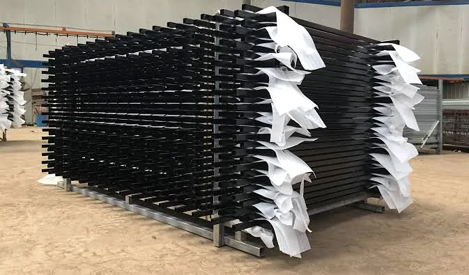 Stacks of black steel fence panels with protective wrap, stored in a warehouse.