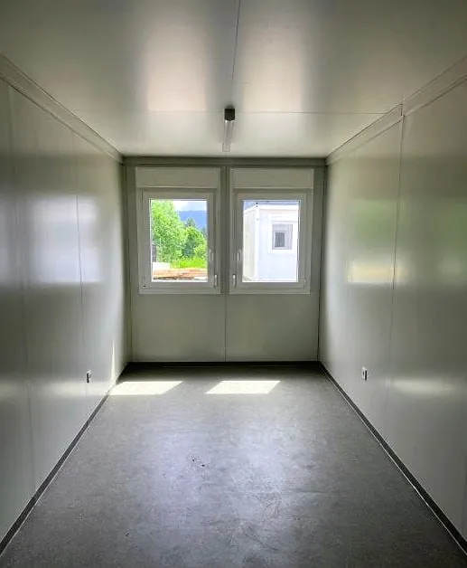 Flatpack building interior with white walls, grey floor and a double window at the end.