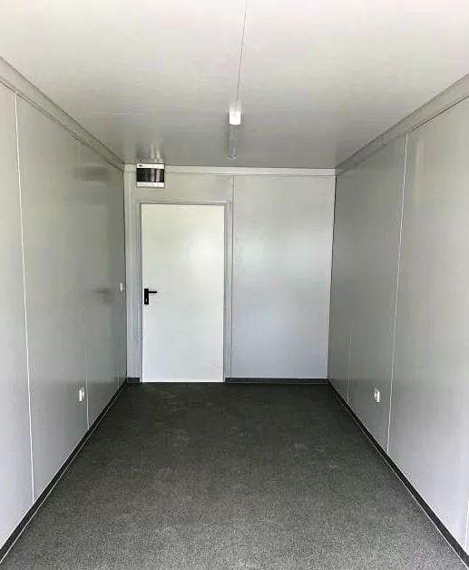 Flatpack building interior with white walls, grey floor and a white door at the end.