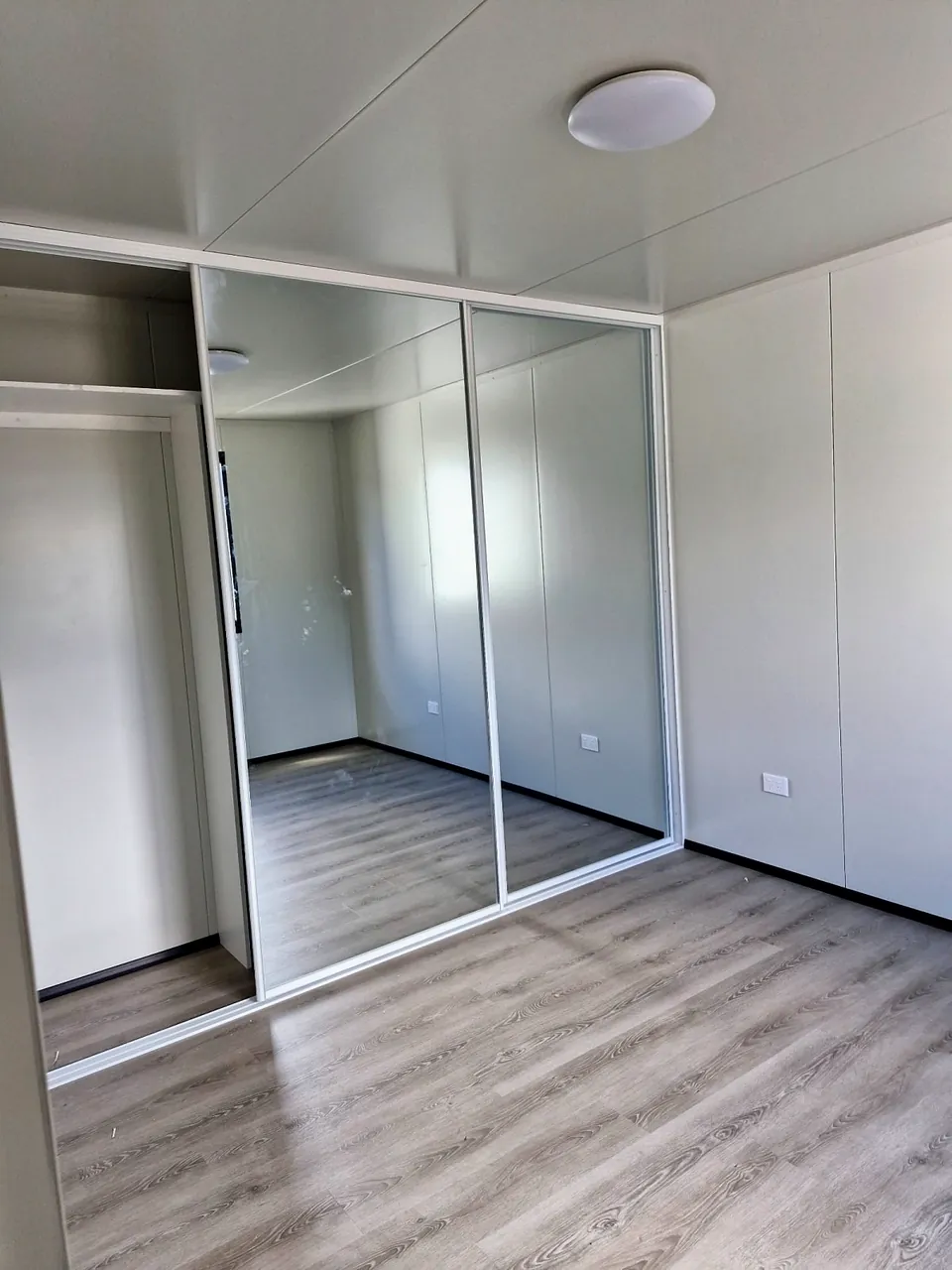 Bedroom with a mirrored sliding wardrobe and timber-look floor.