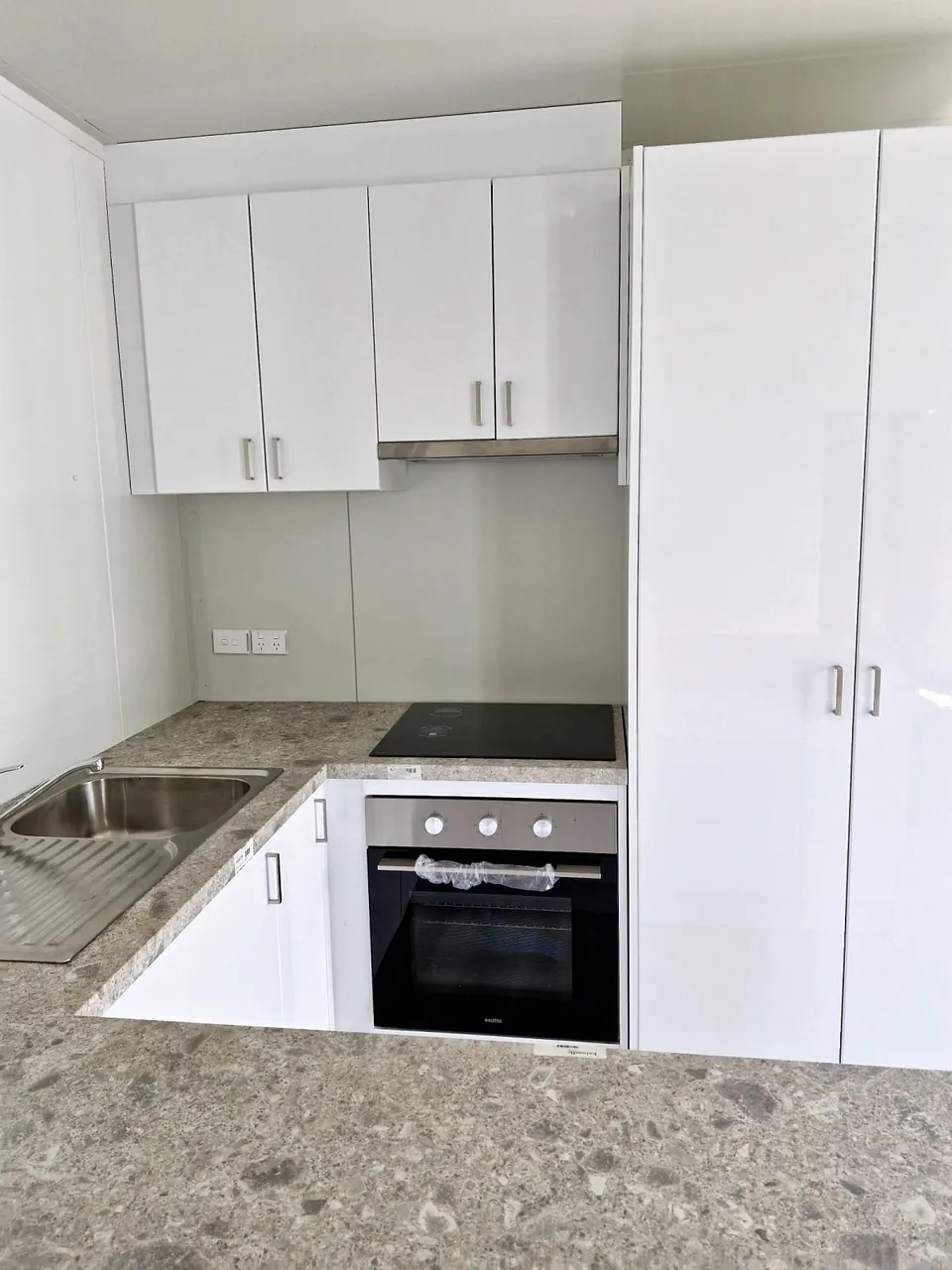 Kitchen with white cabinets, wall oven, cooktop, sink and speckled stone-look benchtop.