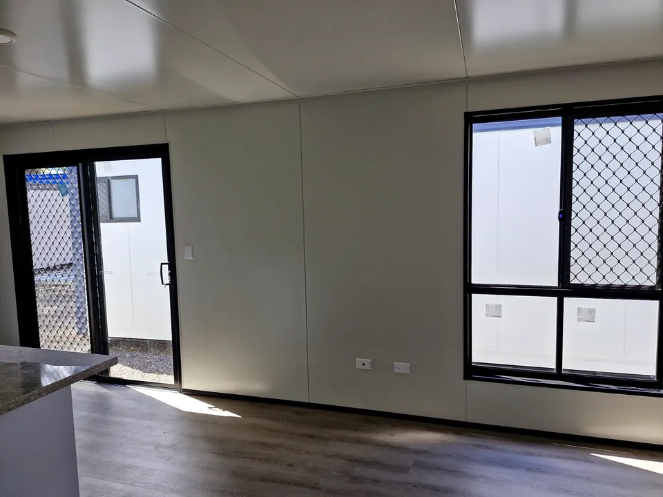 Living area with a glass sliding door and window with security screens, timber-look floor.
