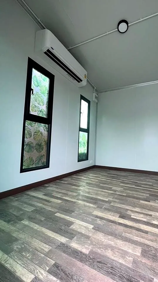 Small room with white walls, split-system air conditioner, tall black windows and timber-look floor.