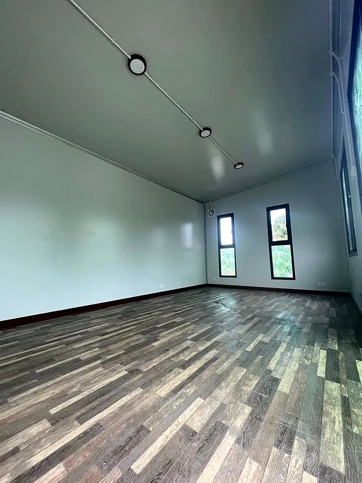 Empty interior with pale walls, sloped ceiling lights and multi-tone plank floor.