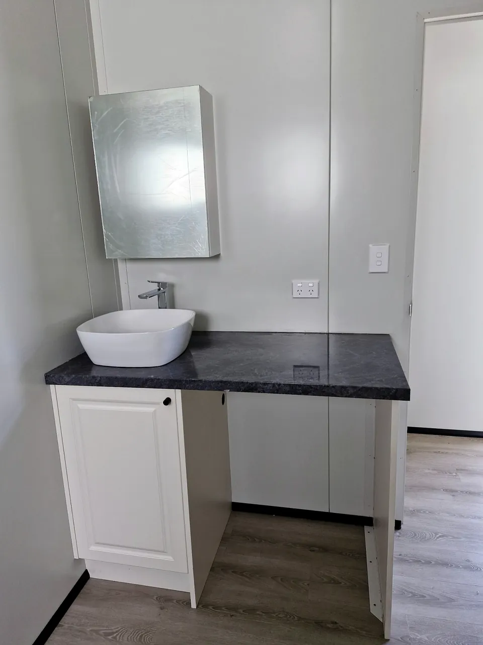 Bathroom vanity with a white vessel basin, dark benchtop and mirror cabinet.