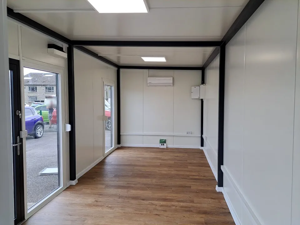Modular office interior with white walls, black frame, timber-look floor, LED panels and a split-system air conditioner.