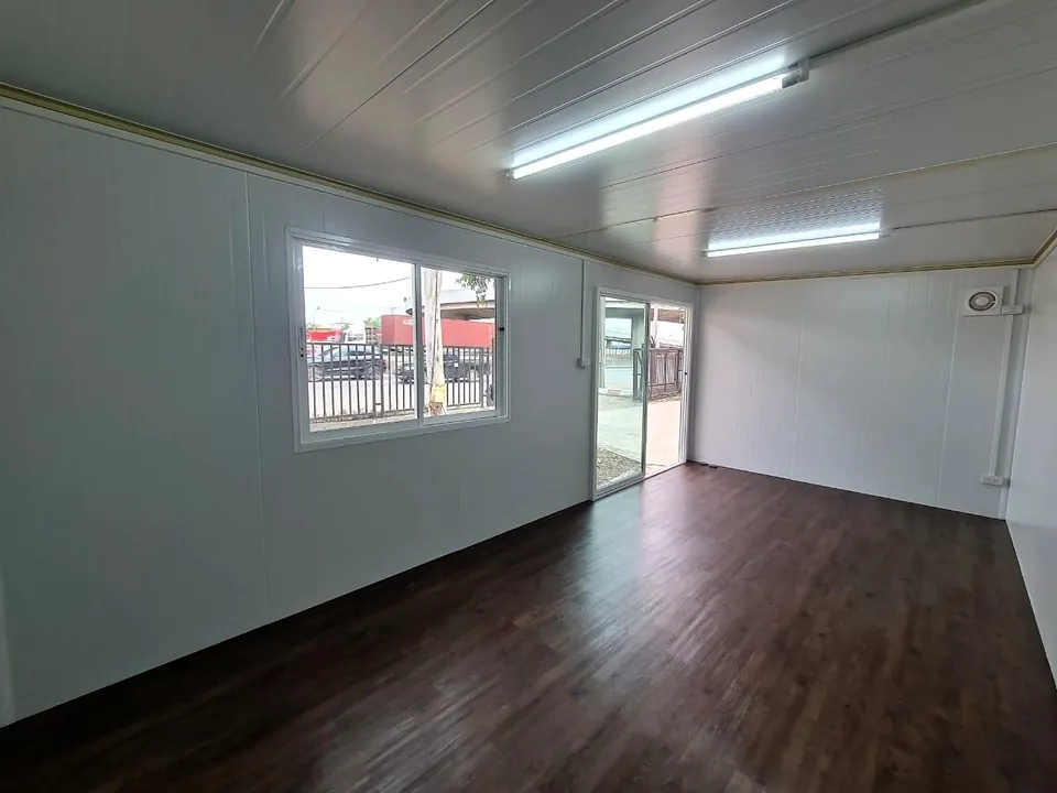 Portable cabin interior with white walls, dark timber-look floor, fluorescent lights and a window looking onto a street.