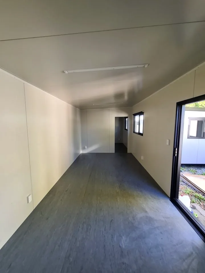 Long portable cabin interior with cream walls, grey floor and a sliding door open to the side.