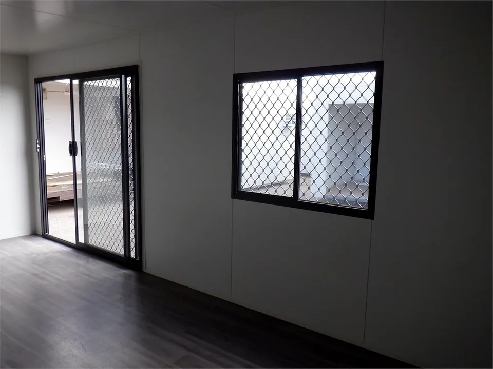 Portable office interior with dark floor, a glass sliding door and window with mesh security screens.