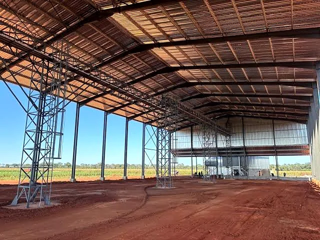 Interior of a very large steel-framed shed with red dirt floor.